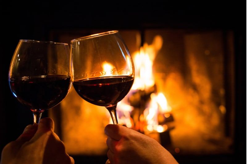 Zwei Weingläser klirren an einem Date-Abend neben einer Feuerstelle