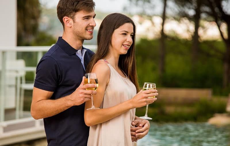 Junges Paar mit Weinprobe am Pool eines Hotels