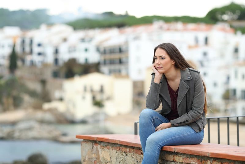Frau schaut weg und sitzt auf einem Felsvorsprung in einer Küstenstadt