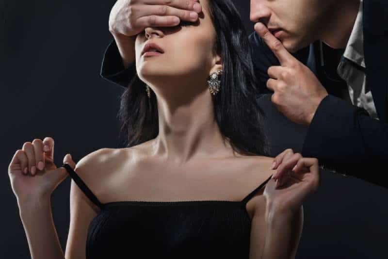 Der Mann zeigt der Frau eine Schweigegeste, während er ihre Augen bedeckt