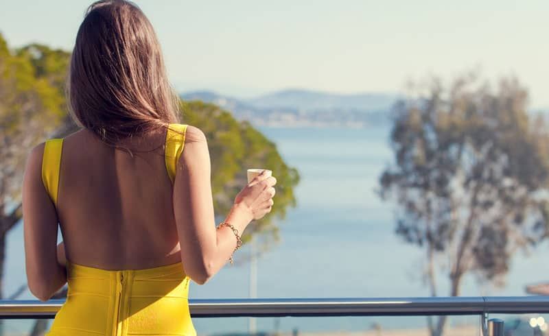 einsame Frau in einem gelben Kleid auf einem Balkon neben Wasser
