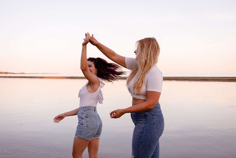 Zwei glückliche Freundinnen tanzen bei Sonnenuntergang am Strand