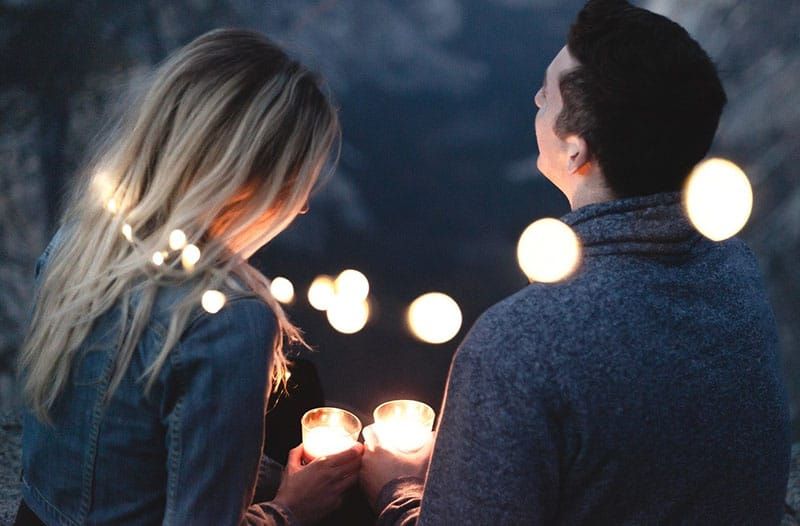 Mann und Frau halten Kerzen, um die herum Reihenlichter aufgestellt sind