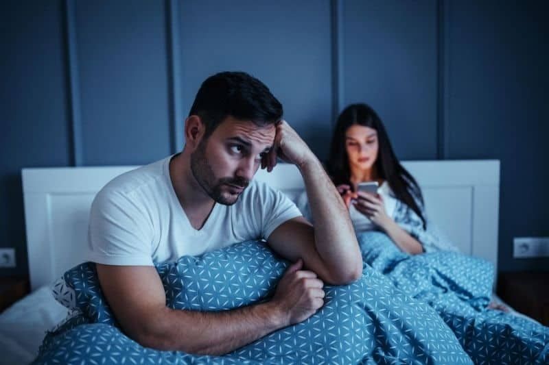 Frau mit Smartphone ignoriert ihren gelangweilten Ehemann im Bett