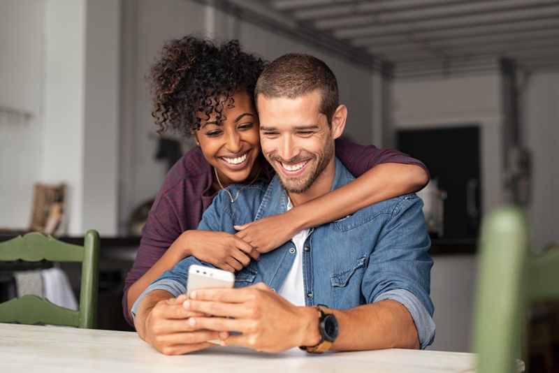 Lächelndes junges Paar umarmt sich, während es auf das Smartphone schaut