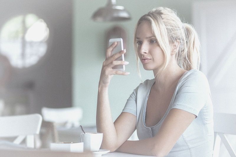 Junge Frau sitzt nachdenklich in einem Café und schreibt SMS