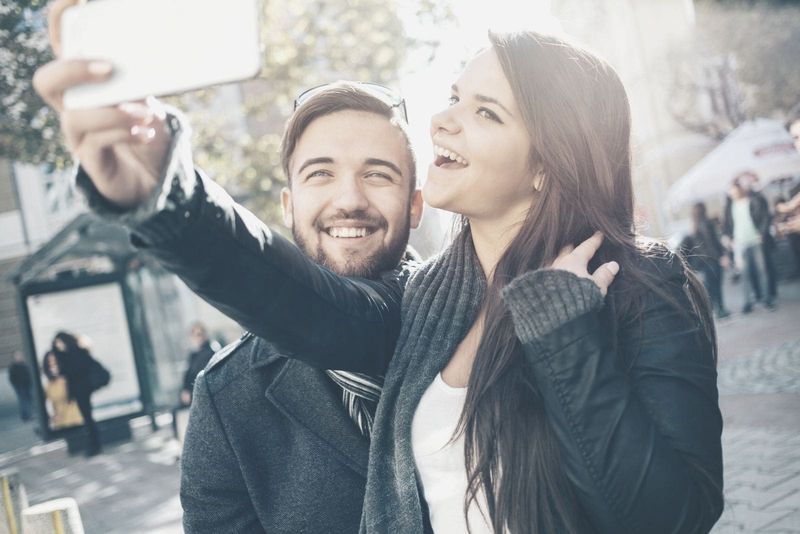 Mann und Frau machen Selfie auf ihrem Smartphone, während sie im Freien spazieren gehen