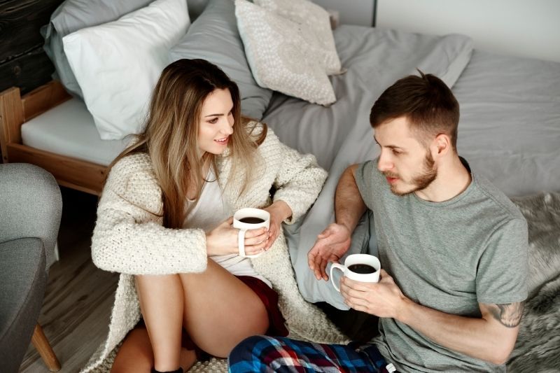 Ein Paar entspannt sich beim Morgenkaffee auf dem Boden neben dem Bett