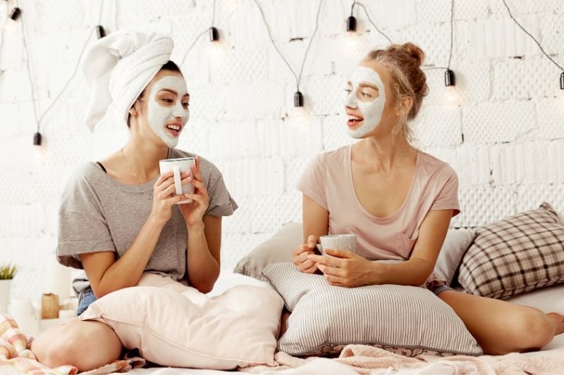 Beste Freunde unterhalten sich mit Kaffee im Schlafzimmer und haben Gesichtsmasken im Gesicht