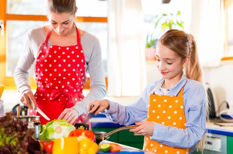 Frau bringt Kind bei, in der Küche mit Schürzen zu kochen