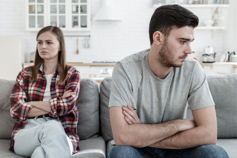 Unglücklicher Mann im grauen T-Shirt und Frau sitzen auf dem Sofa