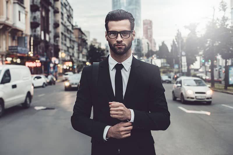Schöner, selbstbewusster Geschäftsmann mit Brille, der mitten auf der Straße steht