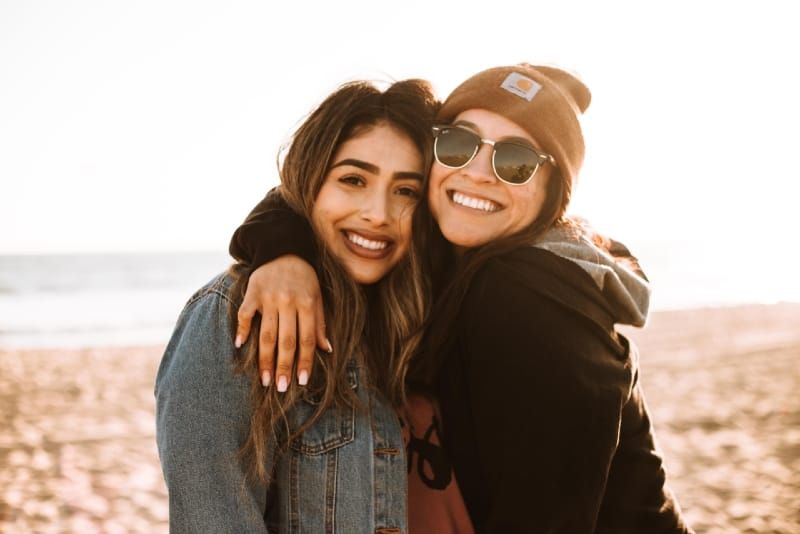 Zwei lächelnde Frauen umarmen sich, während sie am Strand stehen