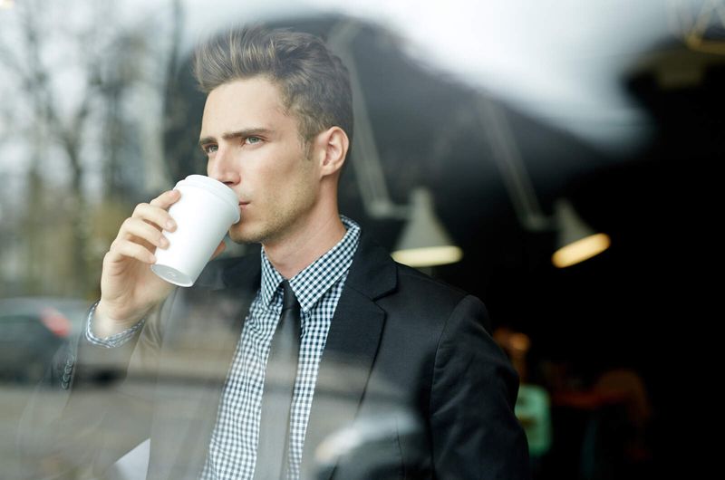 Junger Mann trinkt Kaffee und schaut durch das Fenster