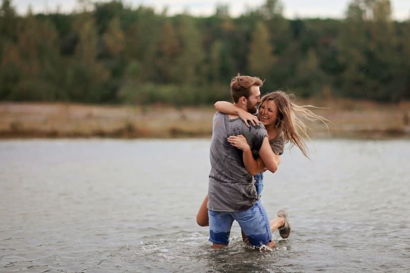 Mann und Frau spielen im Fluss, während der Mann die Frau trägt