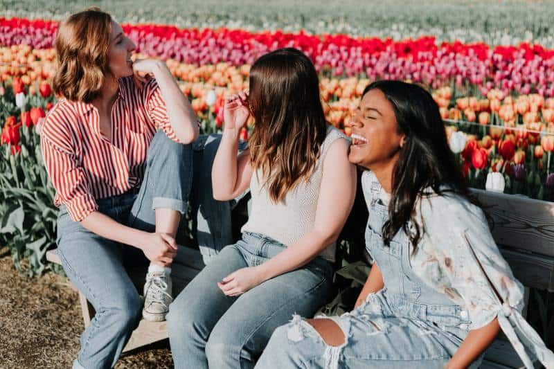 Drei junge Mädchen sitzen auf einer Bank in der Nähe eines bunten Tulpenfeldes