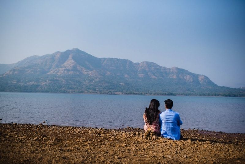 Mann und Frau sitzen am Ufer und schauen aufs Wasser