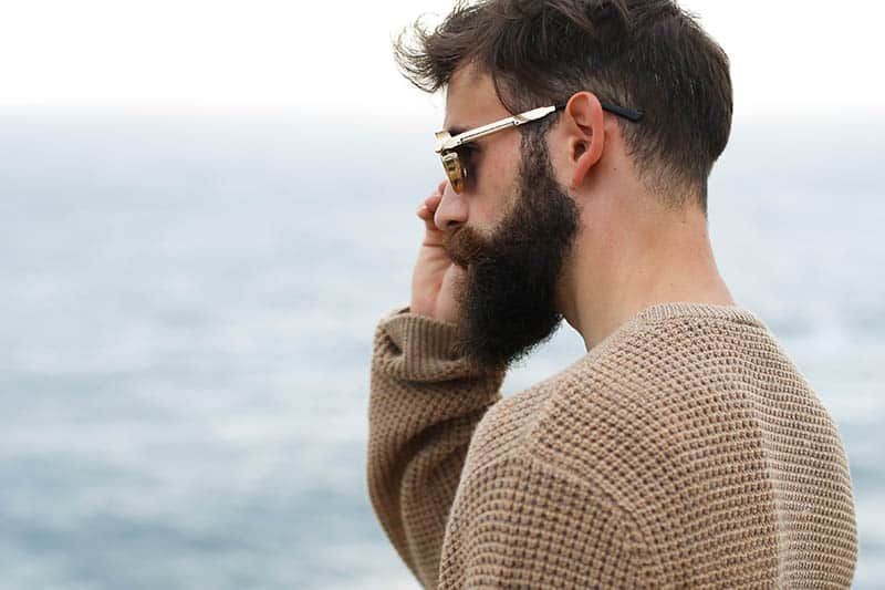 Seitenansicht eines bärtigen Mannes mit Sonnenbrille und braunem Sweatshirt draußen