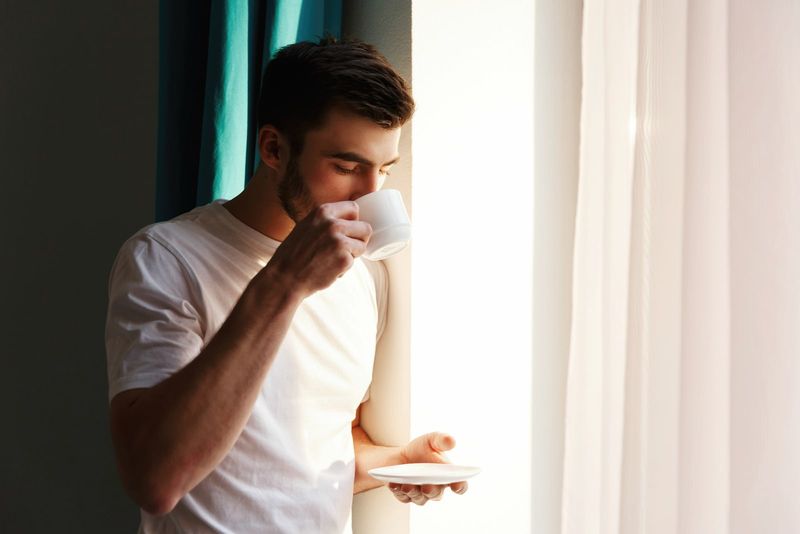 Mann trägt weißes T-Shirt und trinkt Kaffee