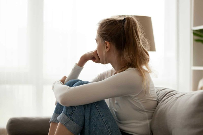 Ein enttäuschtes Mädchen mit zusammengebundenen Haaren sitzt auf der Couch und schaut weg