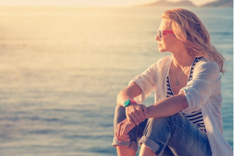 Frau, die in der Nähe des Meeres denkt, sitzt daneben und trägt eine Sonnenbrille
