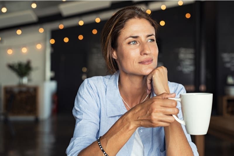 Frau lächelt leicht, während sie eine Tasse Kaffee in einem Café hält