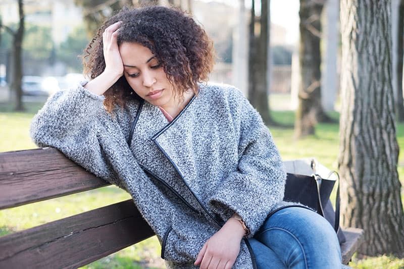 Traurige schwarze Frau sitzt allein auf einer Bank im Park