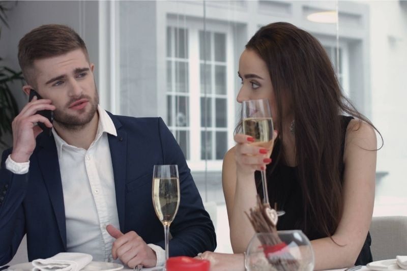 Gelangweilte Frau speist mit ihrem Freund, der gerade telefoniert