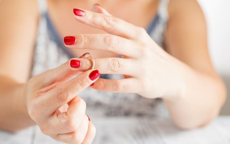 Hände einer Frau mit rotem Nagellack, die den Ehering abnimmt