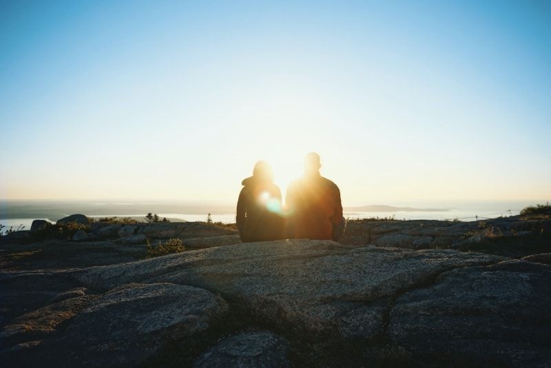 Mann und Frau sitzen auf einem Felsen und schauen auf den Sonnenaufgang