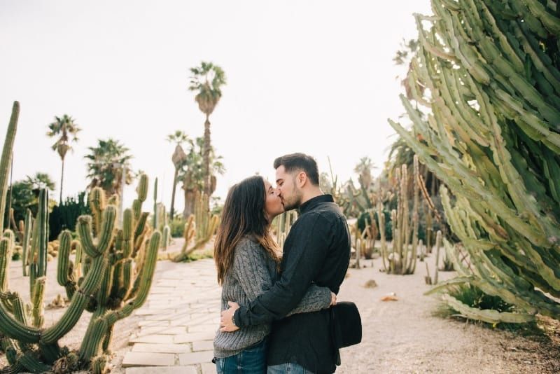 Mann und Frau küssen sich, während sie neben einem Kaktus stehen