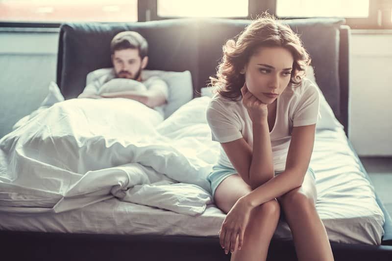 Traurige Frau sitzt auf dem Bett, während der Mann sie ignoriert