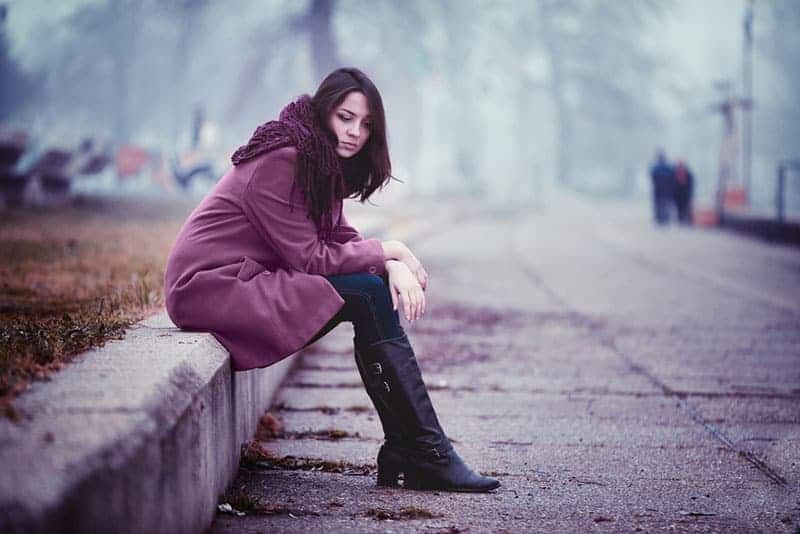 Enttäuschende junge Frau sitzt auf der Steinbrüstung