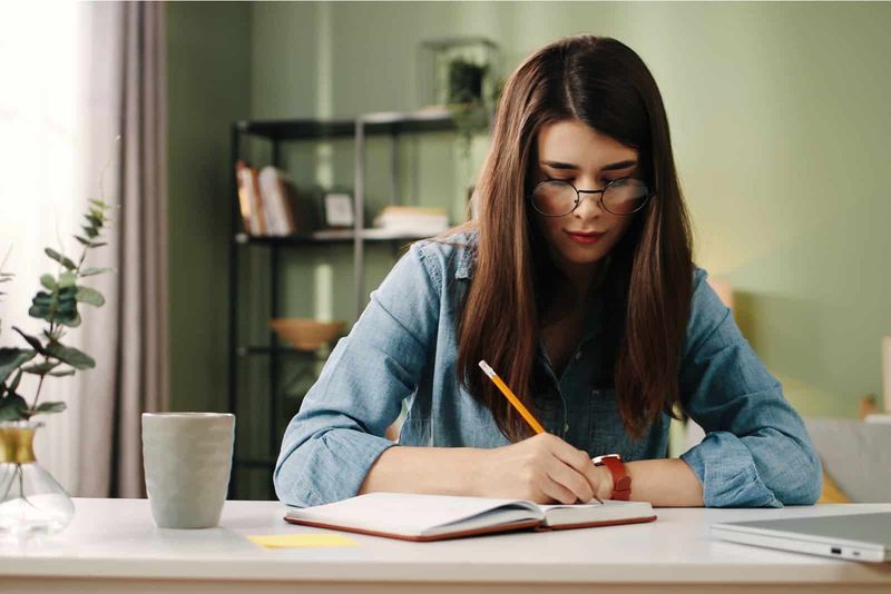 Eine Frau mit langen braunen Haaren sitzt an einem Tisch und schreibt