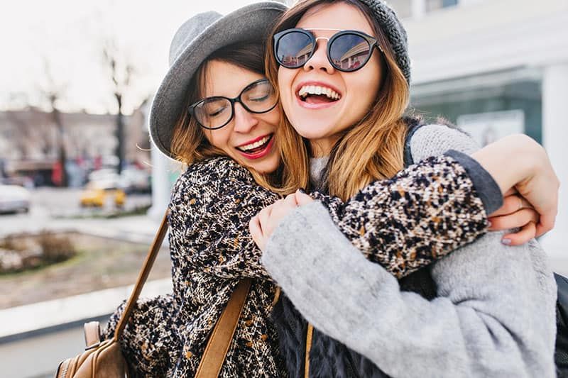 Fröhliche, helle, positive Momente zweier stilvoller Mädchen, die sich auf der Straße in der Stadt umarmen. Nahaufnahme eines Porträts lustiger, fröhlicher, attraktiver junger Frauen, die Spaß haben, lächeln, schöne Momente haben und beste Freunde sind