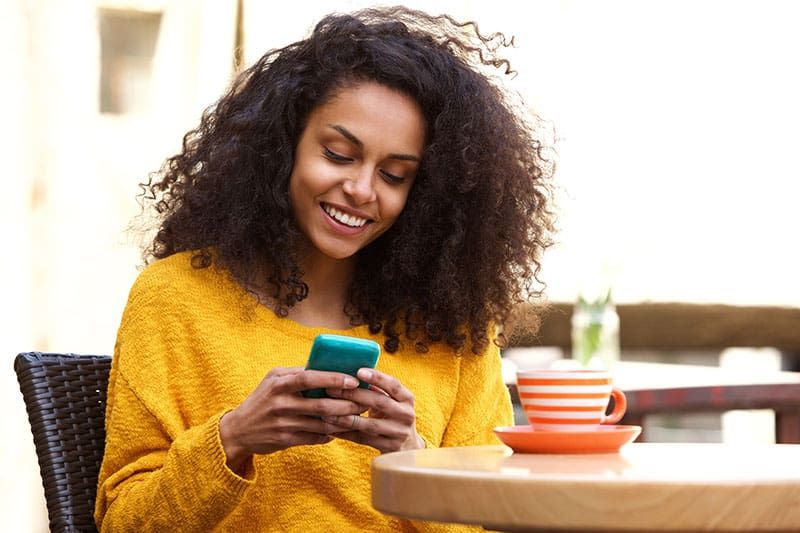 Nahaufnahme des Porträts einer schönen jungen afroamerikanischen Frau, die im Café eine Textnachricht auf dem Mobiltelefon liest