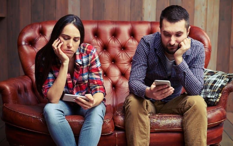 Gelangweiltes Paar schaut auf Telefone und sitzt auf der roten Couch