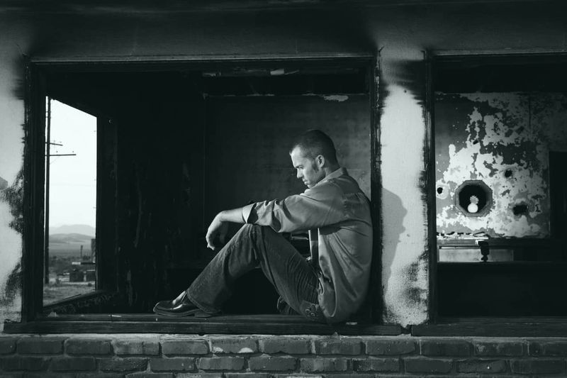 Schwarz-Weiß-Bild eines einsamen, traurigen Mannes, der am Fenster sitzt
