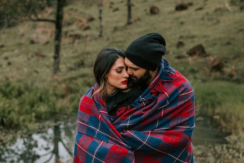 Ein mit einer Decke bedecktes Paar steht in der Nähe eines Sees im Wald