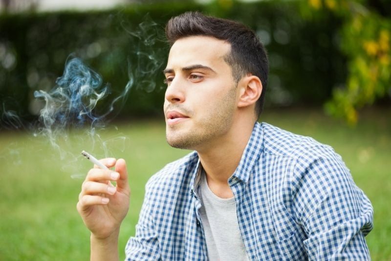 Nachdenklicher Mann, der im Sitzen draußen eine Zigarette raucht