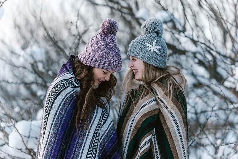 Zwei lächelnde Freundinnen, die im Winter mit einer Decke bedeckt sind