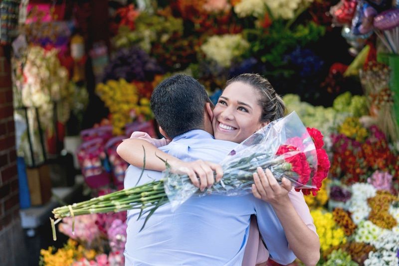 Romantisches Paar, das Blumen schenkt und den Mann in der Nähe des Blumenladens umarmt