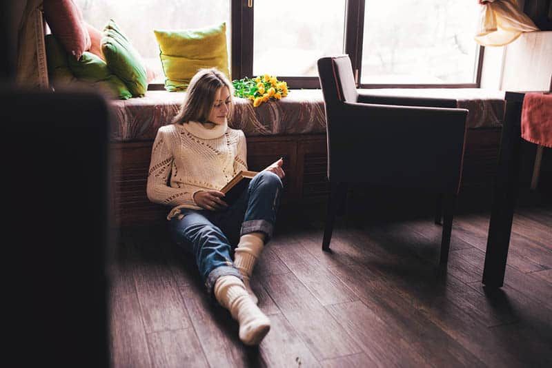Frau liest Buch, während sie auf dem Boden sitzt
