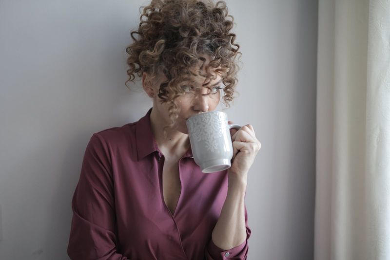 Frau mit lockigem Haar trinkt Kaffee in der Nähe der Wand