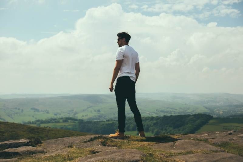 Mann steht auf Felsbrocken mit Blick auf die Hügel und Berge