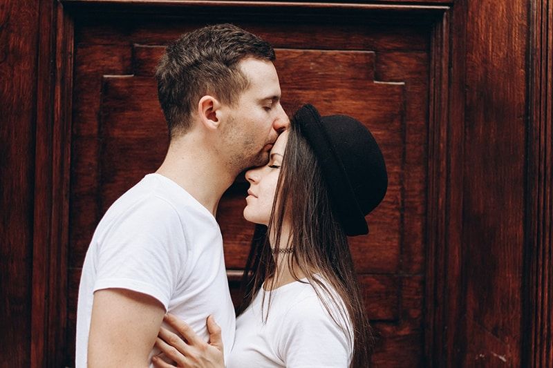 Mann küsst Frau auf die Stirn, während er zusammen in der Nähe der Tür steht