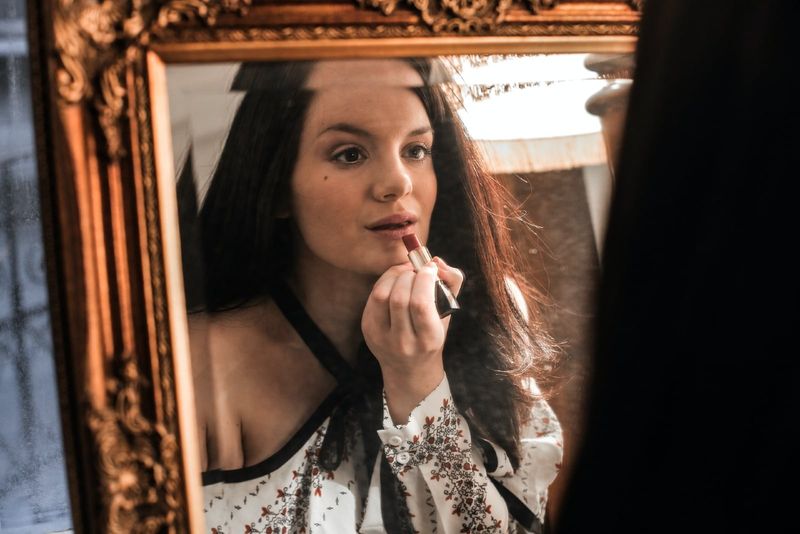 Frau trägt Lippenstift auf, während sie in den Spiegel schaut