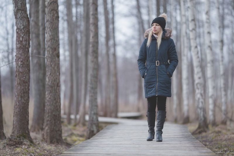 Junge Frau in dunkler, warmer Kleidung, die auf einem Holzweg in einem ruhigen Park spaziert