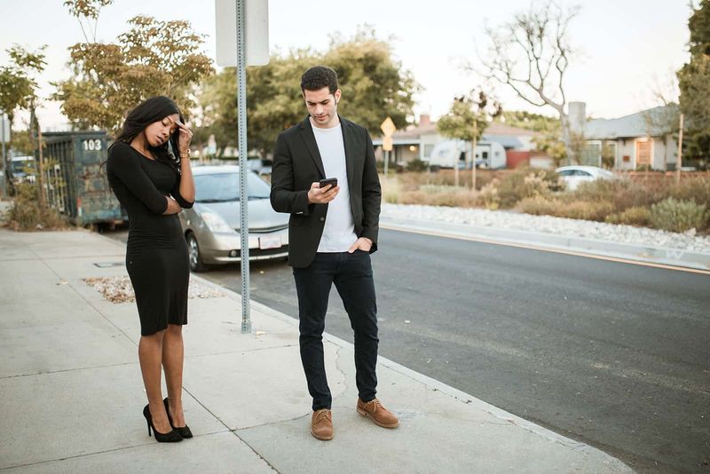 Ein eifersüchtiger Mann checkt das Smartphone seiner Freundin, während er gemeinsam auf dem Bürgersteig steht