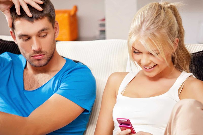 Eifersüchtiger Mann schaut auf das Smartphone seiner Freundin, während sie es benutzt